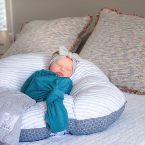 Sleeping newborn in a teal outfit and gray bow resting comfortably on a striped nursing pillow during an indoor professional newborn portrait photography session by Kay Fritze of Fritze Media