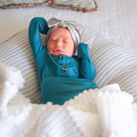 Sleeping newborn in a teal outfit and gray bow resting on striped bedding during a softly lit professional newborn portrait photography session by Kay Fritze of Fritze Media