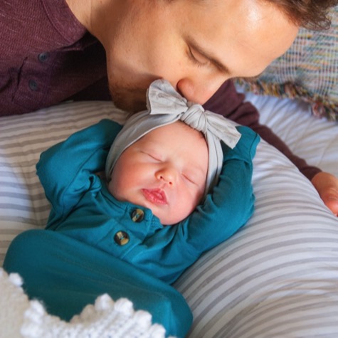 Father gently kissing a sleeping newborn wearing a teal outfit and bow during an intimate professional newborn portrait photography session by Kay Fritze of Fritze Media