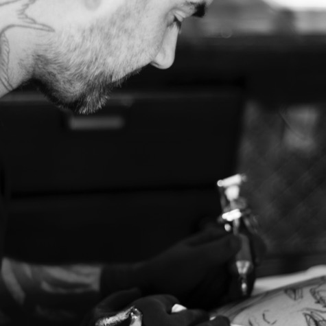 Black-and-white professional branding photo of tattoo artist Doren concentrating while using a tattoo machine on a client's arm