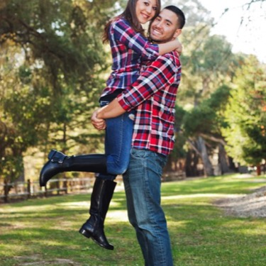 A man and woman in matching red and blue plaid shirts and denim jeans hug and the woman is lifted into the air during a couple's Valentine's Day portrait photography session by Kay Fritze of Fritze Media