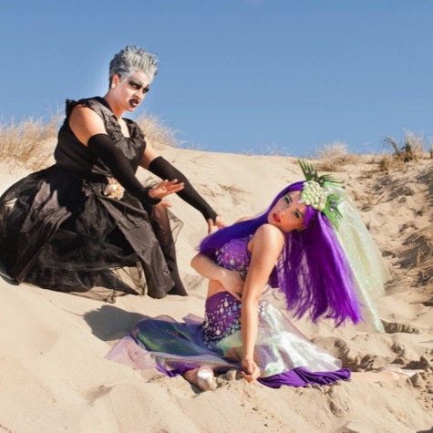 Two women in dramatic black and purple fantasy costumes posing among coastal sand dunes during a creative professional portrait photography session by Kay Fritze of Fritze Media