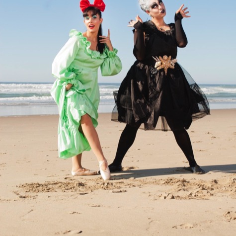 Two women in theatrical green and black costumes posing together on an ocean beach during a creative professional portrait photography session by Kay Fritze of Fritze Media