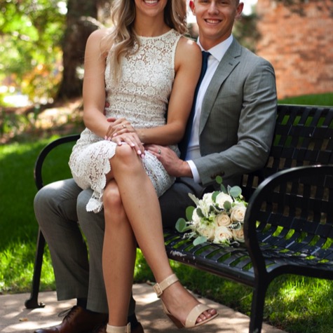 Couple in formal attire seated together on a park bench with a floral bouquet during a professional couples wedding engagement portrait photography session by Kay Fritze of Fritze Media