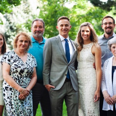 Engaged couple in formal attire surrounded by members of their extended family outdoors during a professional engagement and family portrait photography session by Kay Fritze of Fritze Media