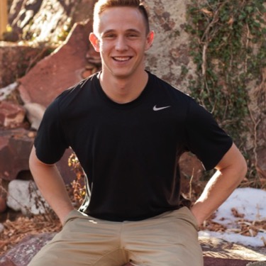 Young man in a black athletic shirt seated beside landscaped rocks and smiling at the camera during an outdoor professional individual portrait photography session by Kay Fritze of Fritze Media