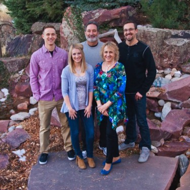 Family of five standing together beside a landscaped rock waterfall during an outdoor professional family portrait photography session by Kay Fritze of Fritze Media