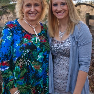 Mother and adult daughter smiling together outdoors beside landscaped rocks during a professional mother-daughter portrait photography session by Kay Fritze of Fritze Media