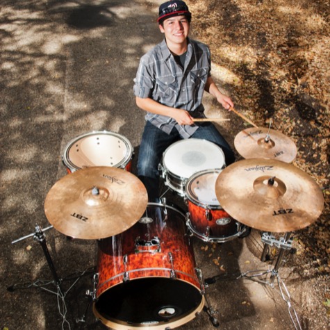 Professional musician portrait of a smiling drummer playing a red drum kit outdoors beneath trees photographed from above by Kay Fritze of Fritze Media