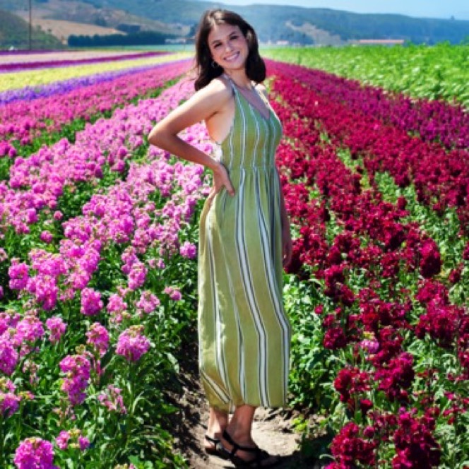 Woman in a striped dress standing in a vibrant field of pink flowers during a professional outdoor portrait session by Kay Fritze of Fritze Media