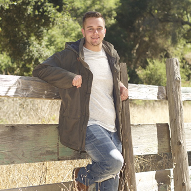Man in a casual jacket leaning against a white wooden fence during an outdoor professional portrait photography session by Kay Fritze of Fritze Media