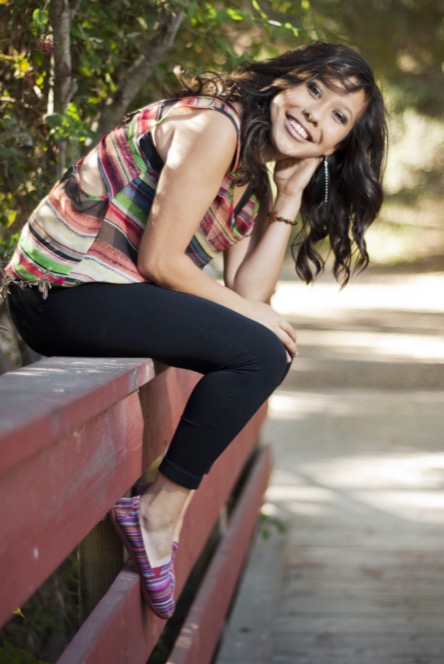 Woman in a colorful striped top leaning beside a red bench during a relaxed outdoor professional portrait session by Kay Fritze of Fritze Media