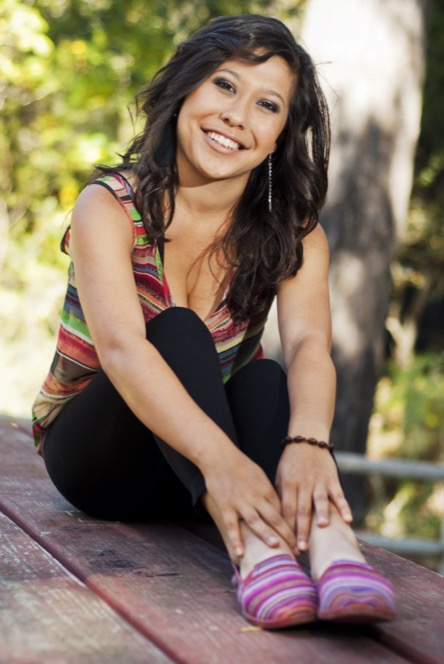 Woman in a colorful striped top posing beside a red wooden bench during an outdoor professional portrait photography session by Kay Fritze of Fritze Media