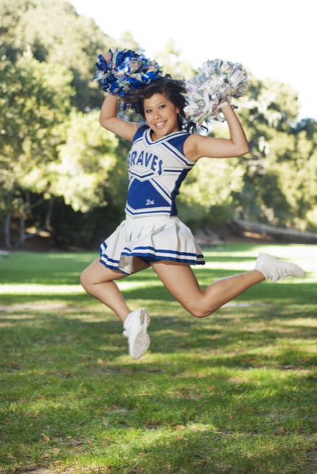Cheerleader in a blue uniform jumping on a grassy field during an energetic professional portrait photography session by Kay Fritze of Fritze Media