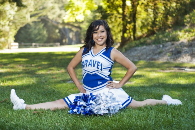 Cheerleader in a blue uniform posing with pom-poms on a grassy field during a professional portrait session by Kay Fritze of Fritze Media