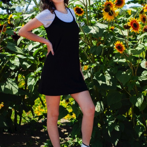 Young woman in a black dress and white high-top shoes posing among tall sunflowers during an outdoor professional senior portrait photography session by Kay Fritze of Fritze Media