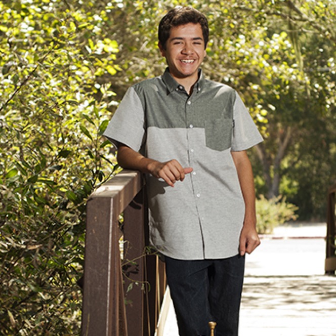 Young man in a gray polo posing beside a white brick wall during a professional senior portrait photography session by Kay Fritze of Fritze Media