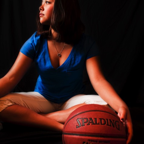 Professional sports portrait of a woman in a blue shirt seated against a black background with a Spalding basketball beside her