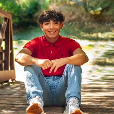 Young man in a black T-shirt seated at a wooden picnic table during an outdoor professional portrait session by Kay Fritze of Fritze Media