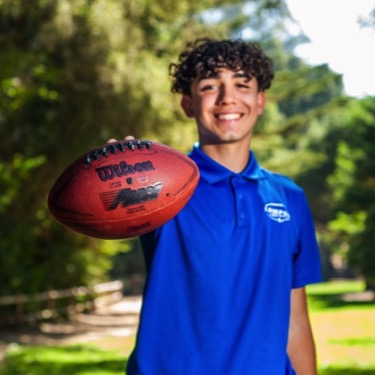 Young man in a blue polo holding a football outdoors during a professional senior portrait photography session by Kay Fritze of Fritze Media