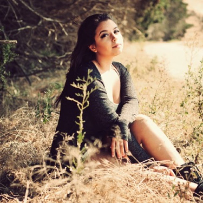 Woman in a dark outfit seated among tall grass and woodland during an artistic professional portrait photography session by Kay Fritze of Fritze Media