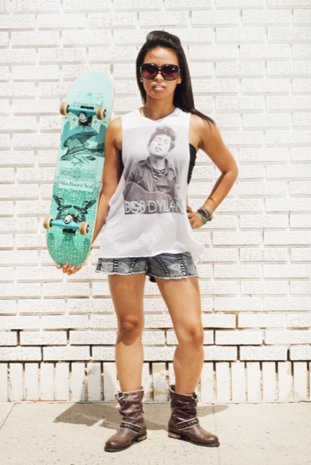 Woman holding a turquoise skateboard beside a white brick wall during a creative professional lifestyle portrait session by Kay Fritze of Fritze Media