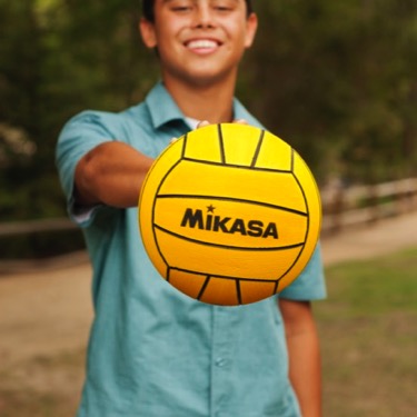 Young man in a green polo holding a yellow volleyball outdoors during a professional senior portrait photography session by Kay Fritze of Fritze Media