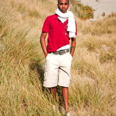 Young man in a red polo and khaki shorts standing in tall grass during an outdoor professional portrait photography session by Kay Fritze of Fritze Media