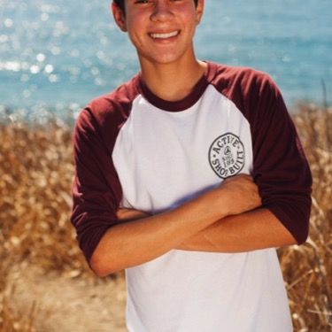 Young man in a baseball-style shirt posing with arms crossed beside the water during an outdoor portrait session by Kay Fritze of Fritze Media