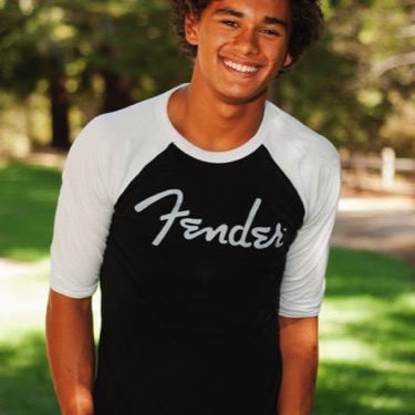 Young man wearing a black-and-white Fender shirt smiling outdoors during a professional portrait photography session by Kay Fritze of Fritze Media