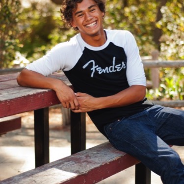 Young man in a Fender shirt seated at a wooden picnic table during an outdoor professional portrait session by Kay Fritze of Fritze Media